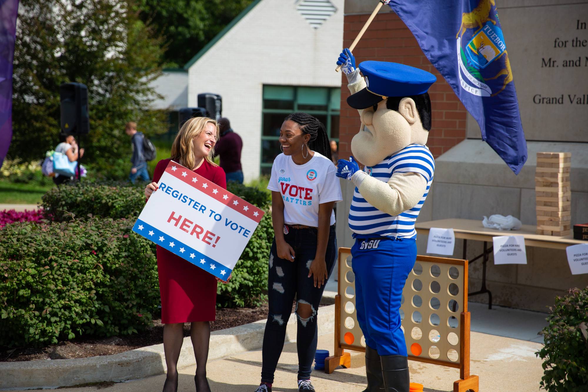 Student holding sign that reads "Register to vote here!" talks to Louie the Laker